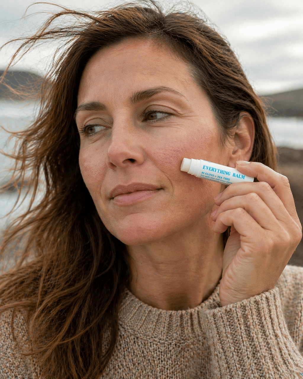 Woman applying Everything Balm to dry cheek outdoors